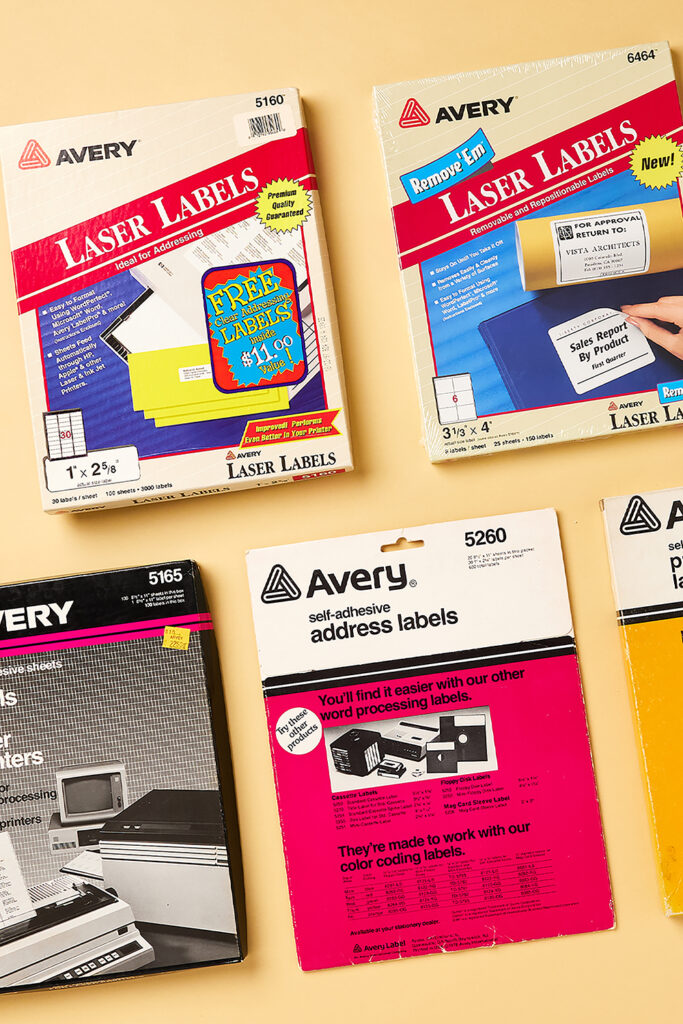 The image showcases a collection of vintage Avery label packaging, representing different moments in the history of labels. It includes various types of laser and self-adhesive address labels. The top left box is for Avery 5160 Laser Labels, featuring a bright red banner and a promotional offer for free labels. To the right is the Avery 6464 Remove 'Em Laser Labels, designed for removable and repositionable use. The bottom section shows Avery 5165 full sheet labels in a black box, and Avery 5260 self-adhesive address labels, highlighting ease of use with word processing systems. These products reflect the evolution of labels in office and personal use over time.