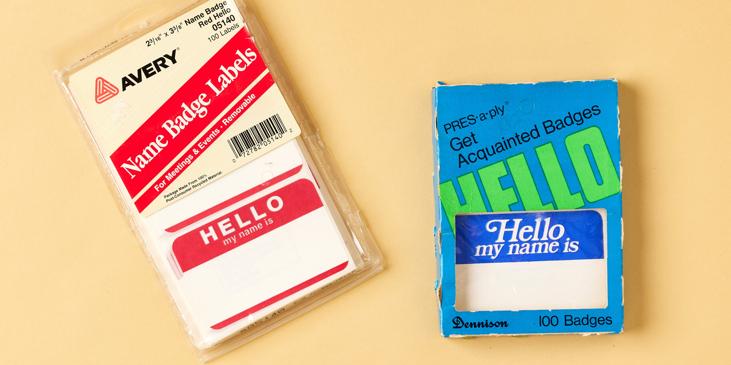 The image features two classic name badge label packages from Avery and Dennison. On the left is an Avery pack of "Name Badge Labels" in red, featuring the well-known "Hello, my name is" design, perfect for meetings and events. Avery, a label maker famous for name tags, emphasizes the removability and eco-friendly material of the product. On the right is a blue "Hello, my name is" badge package from Dennison, containing 100 badges with a similar blue and green design. These items highlight the long-standing use of name tags in both professional and social settings.