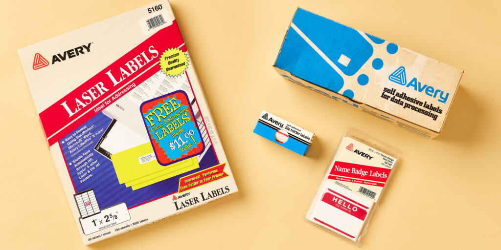 The image displays a collection of old stickers from Avery, highlighting different types of stickers. On the left is a pack of Avery 5160 Laser Labels, ideal for addressing, with a promotional offer for free clear labels. To the right, there is a vintage Avery box for "self-adhesive labels for data processing," showing how labels were packaged for office use. Below that, there are smaller packs of Avery file folder labels and name badge labels, including the iconic "Hello, my name is" design. These items showcase various Avery stickers used for organization, labeling, and name tags throughout the years.