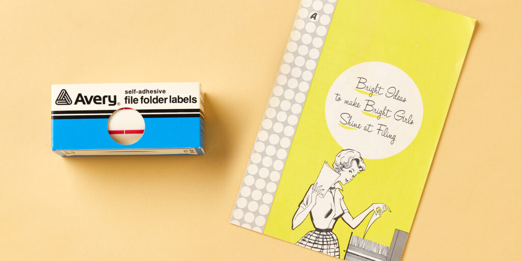 The image features vintage packaging for Avery self-adhesive file folder labels and an old instructional booklet. On the left is a small blue and white box labeled "Avery self-adhesive file folder labels," showcasing its simple retro design. To the right is a bright yellow vintage paper goods booklet with the title, "Bright Ideas to Make Bright Girls Shine at Filing." The cover includes a 1950s-style illustration of a woman organizing files, adding to the nostalgic feel of both products.