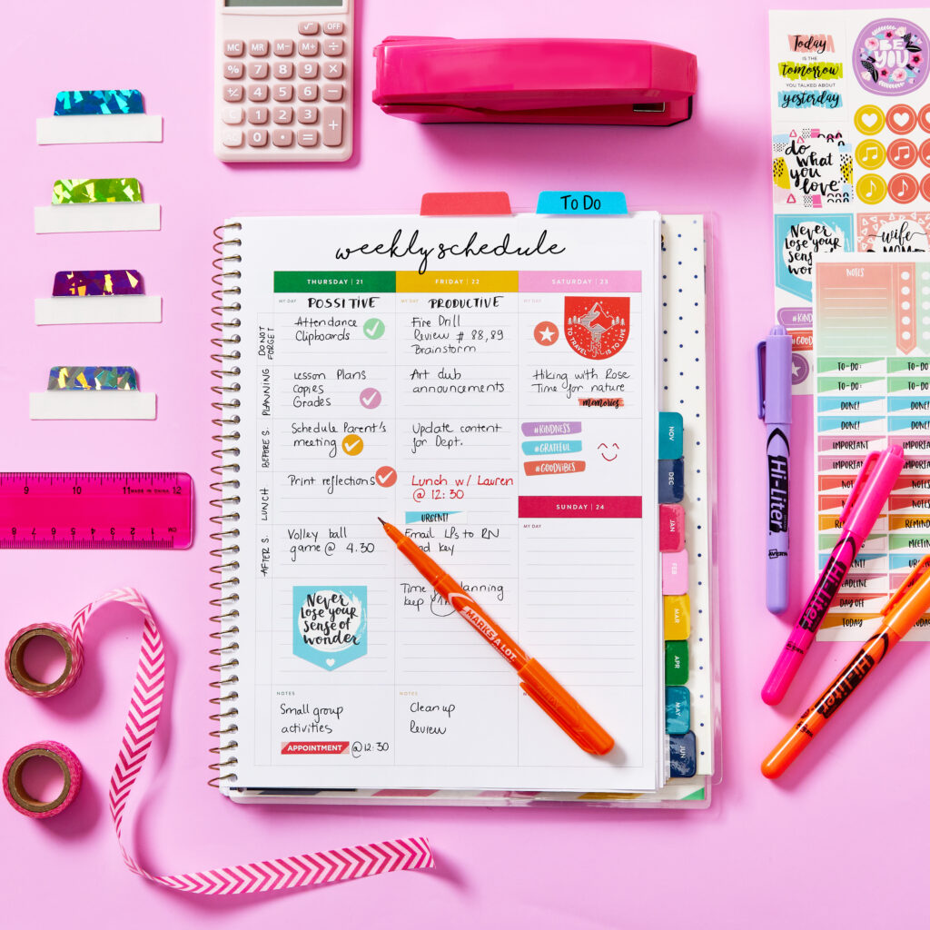 A colorful and organized weekly schedule with Avery Ultra Tabs dividing sections for tasks and notes. The spread features vibrant highlighters, stickers, and decorative elements for categorizing activities like appointments, deadlines, and reminders. Surrounding the schedule are tools such as a pink stapler, ruler, tape, and a calculator, showcasing a visually appealing and functional method for staying on top of tasks