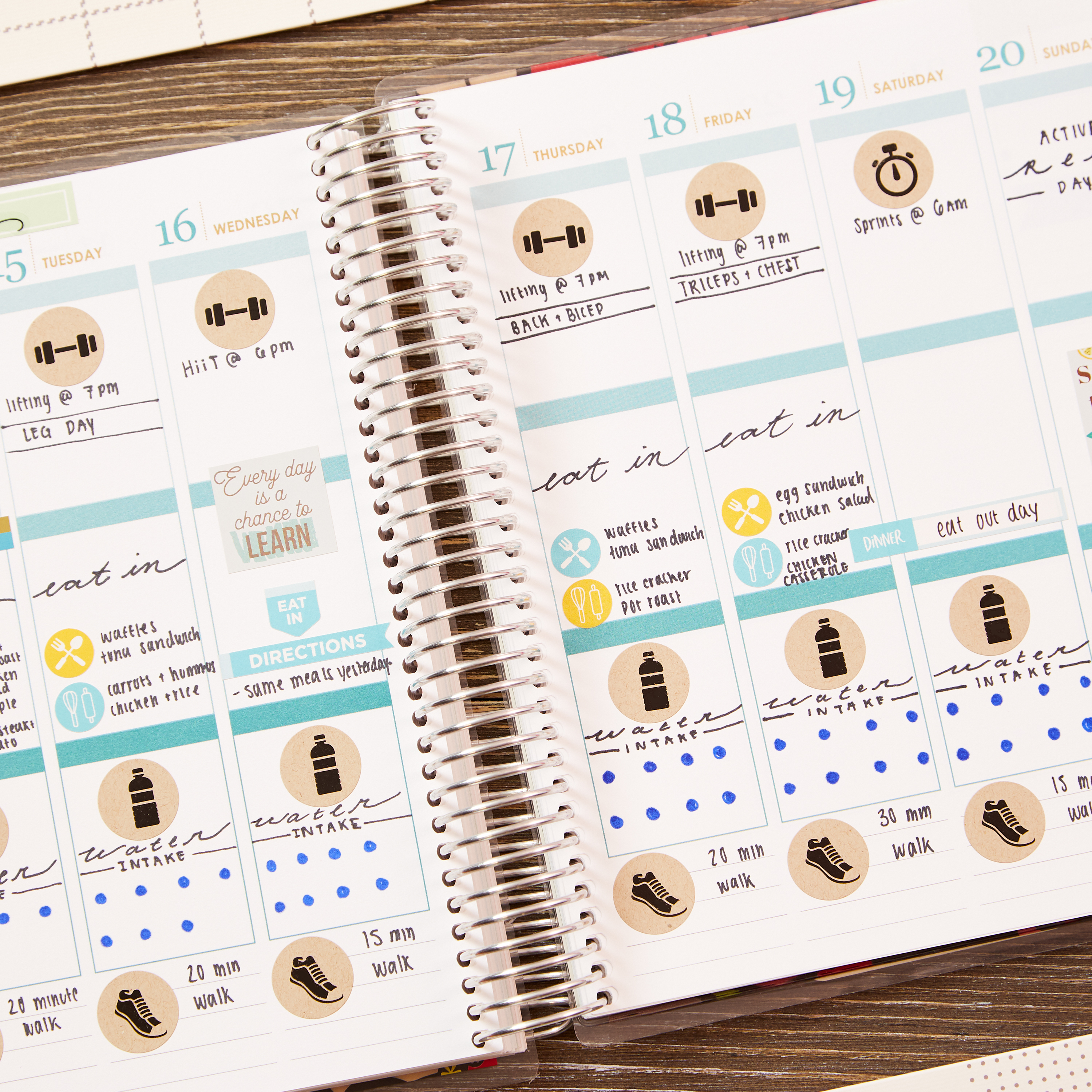 An open spiral-bound planner showcasing a detailed weekly schedule enhanced with free Avery planner sticker designs. The pages include meal plans labeled "eat in," daily water intake trackers with bottle icons and dots for progress, and fitness activities like lifting, HIIT, and walking. Stickers such as dumbbells, shoes, and motivational quotes like "Every day is a chance to learn" add functionality and inspiration. This planner idea demonstrates how to organize workouts, meals, and hydration goals effectively using Avery’s customizable sticker designs.
