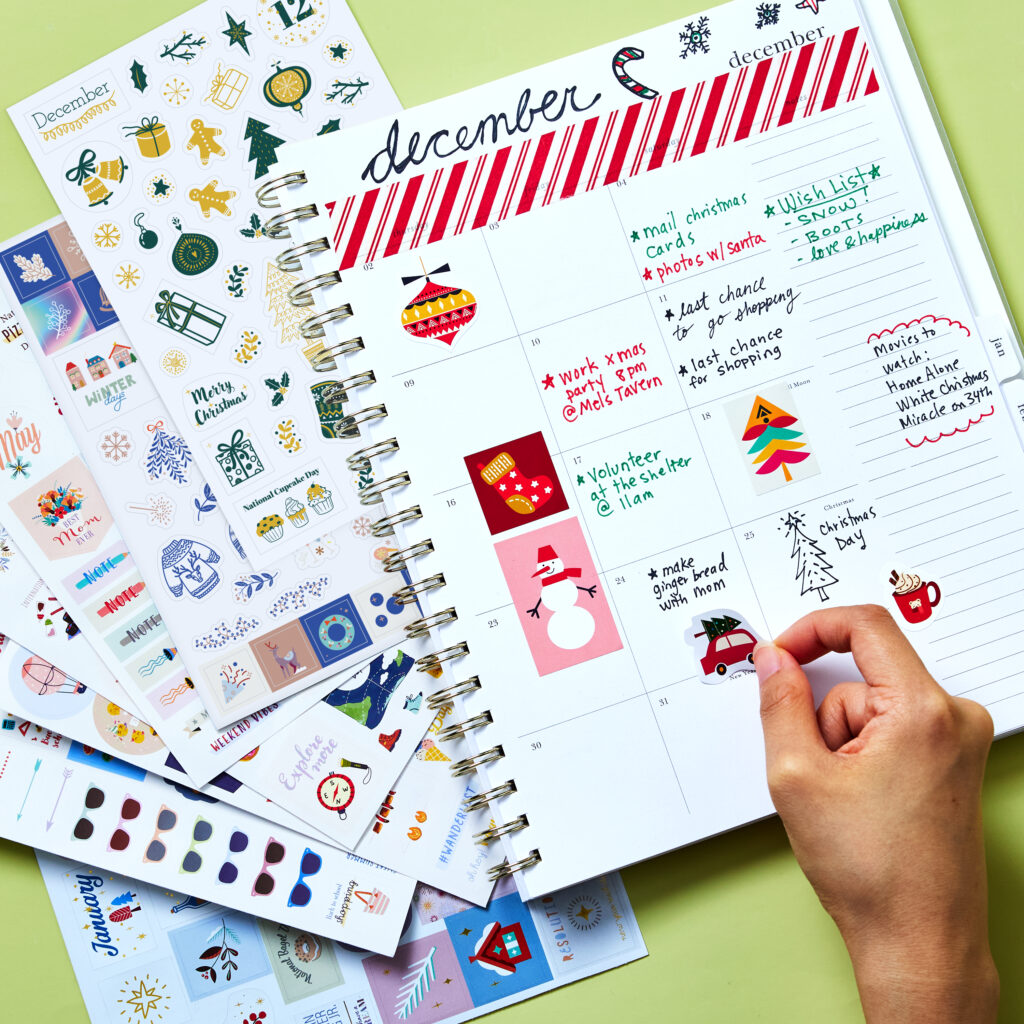 A festive December calendar decorated with Avery 6776 Holiday and Seasons planner stickers, featuring designs like ornaments, snowmen, and Christmas trees. The layout includes handwritten reminders for events, to-do lists, and holiday movies to watch. Surrounding the calendar are additional sticker sheets with seasonal themes, adding color and cheer. This creative setup provides a fun and festive planner idea for organizing holiday activities and celebrations.