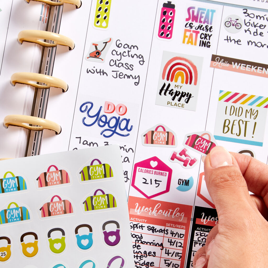 A close-up of a fitness planner showcasing Avery 6787 fitness planner stickers. The planner features handwritten workout schedules, such as "6am cycling class with Jenny" and "Do Yoga," alongside colorful stickers like gym bags, kettlebells, and motivational phrases like "My Happy Place" and "I Did My Best!" A workout log tracks activities, sets, and reps, with stickers for calories burned and gym time. This vibrant planner idea highlights how to use decorative and functional stickers to organize fitness goals and stay motivated.